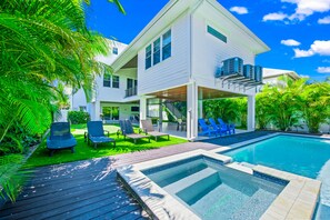Una casa de dos pisos con piscina, mobiliario exterior y abundante vegetación.