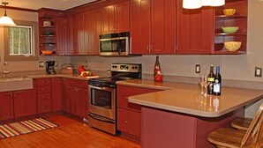 Una cocina con gabinetes de madera, microondas, horno, estufa y una zona de bar con botellas.