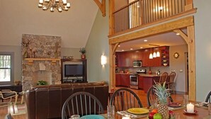 Un comedor con chimenea de piedra, televisor y cocina al fondo.