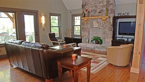 Una sala de estar con chimenea de piedra, un sofá de cuero, una mesa de centro de madera y un televisor.