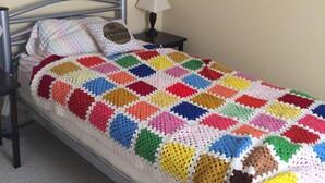 A neatly made bed with a colorful crocheted blanket, a bedside lamp, and a framed picture on the wall. - Spacious and comfortable 5 bedroom, 2 1/2 bath two miles from down town Geneva (Geneva)