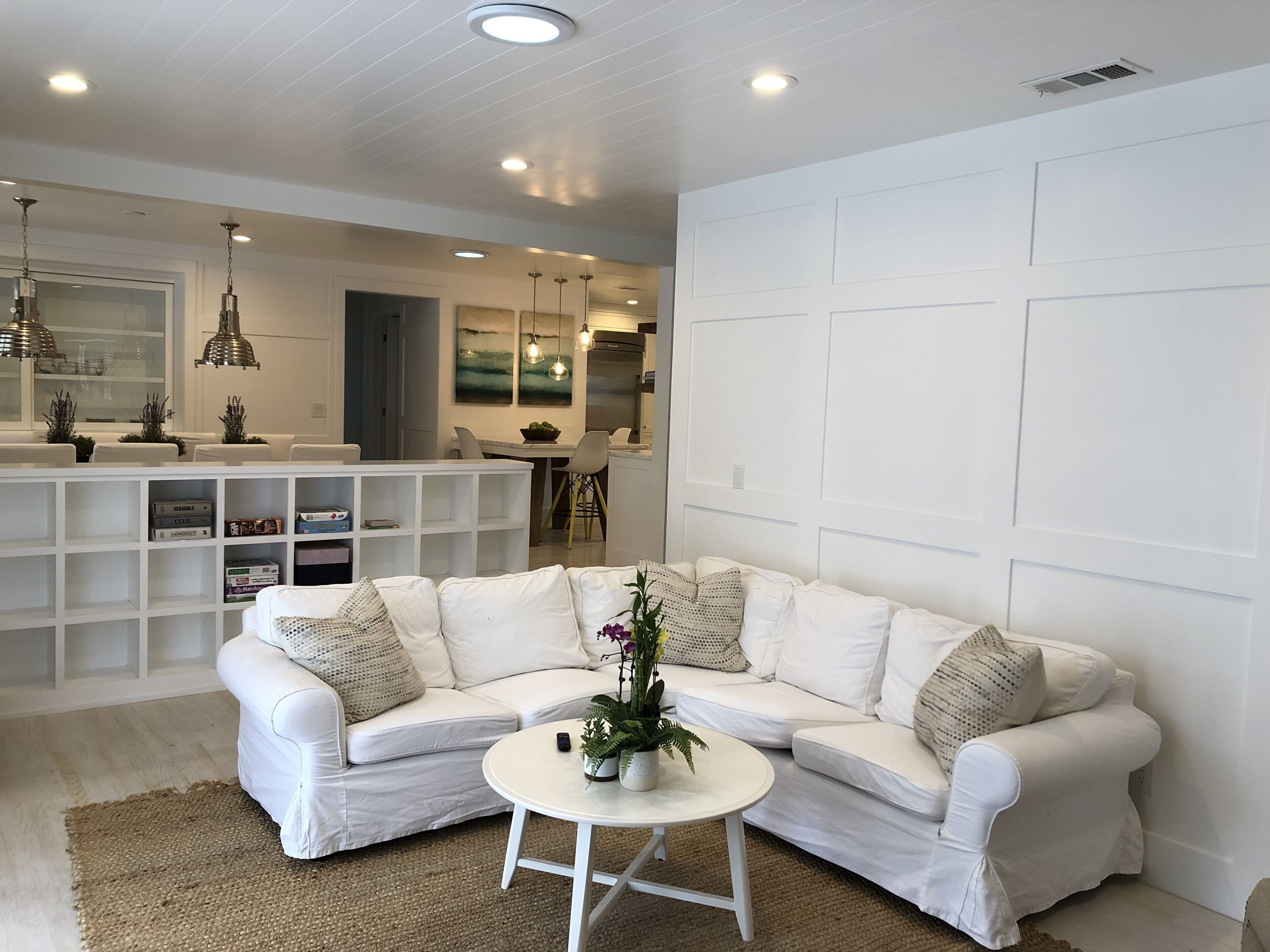 A modern living room with a white sectional sofa, a small white coffee table, and a kitchen area in the background.