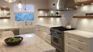 Een moderne keuken met een ruime kookplaat, witte kasten en hanglampen.