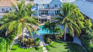 Una casa grande con piscina, rodeada de palmeras y un campo de golf.