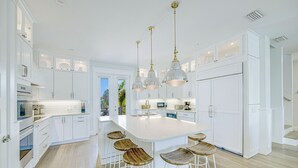 Cocina moderna con armarios blancos, una isla grande con taburetes e iluminación colgante.