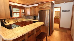Una cocina con gabinetes de madera, un refrigerador de acero inoxidable, encimeras de granito y una estufa empotrada.