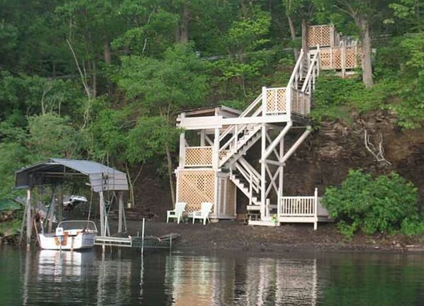A dock with a covered boat house and a wooden staircase leading to a deck.