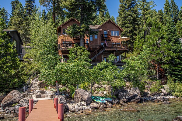 A multi-story lodge with a wooden exterior, a deck, and a clear view of a river.