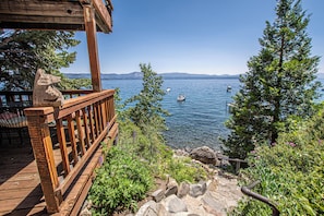 A wooden deck overlooking a lake with boats, surrounded by greenery and a stone wall.