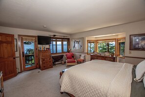 A bedroom with a large bed, wooden furniture, a television, and windows with a view of the outdoors.