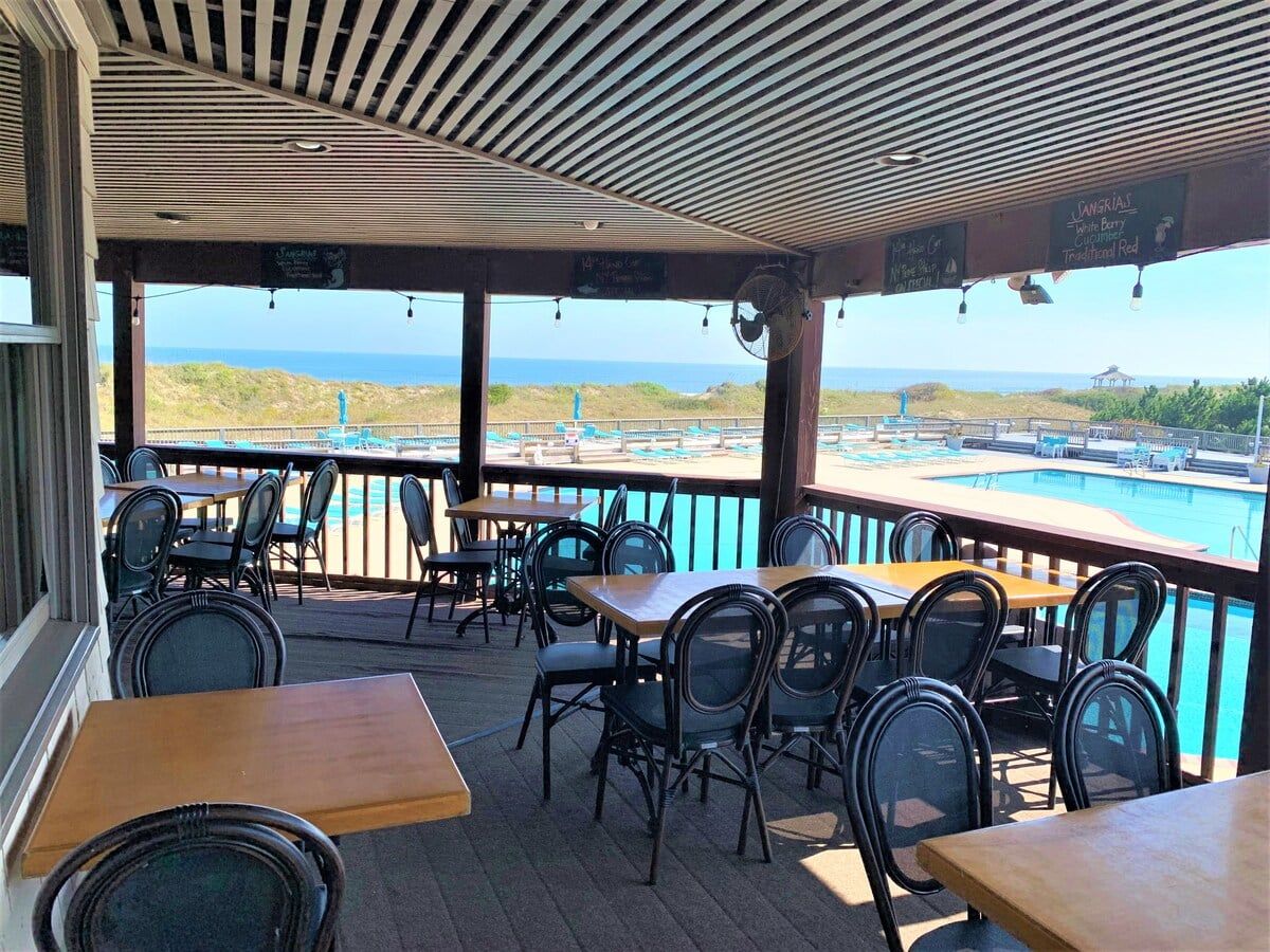 An outdoor seating area with tables and chairs, overlooking a pool and beach.