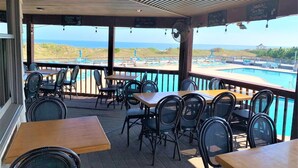 An outdoor seating area with tables and chairs, overlooking a pool and beach. - 5BR Corolla Light retreat with pool, hot tub & beach access. CL-134 (Corolla)