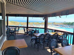 An outdoor seating area with tables and chairs, overlooking a pool and beach.