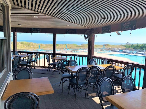 An outdoor seating area with tables and chairs, overlooking a pool and beach.