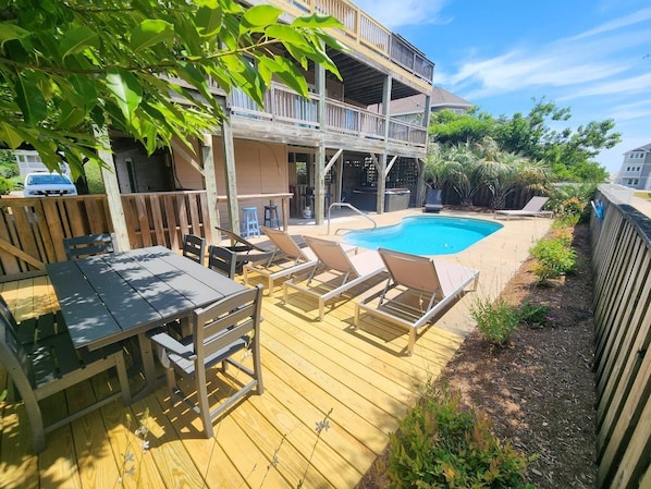 A wooden deck with a pool, lounge chairs, and a table.
