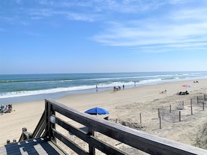 A beach with a wooden boardwalk, umbrellas, and people.