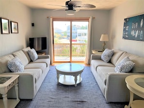 A living room with two sofas, a coffee table, a TV, and a balcony with a view.