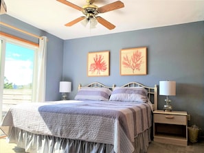 A bedroom with a bed, two bedside tables with lamps, a ceiling fan, and two framed pictures on the wall.