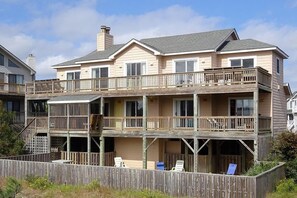 A multi-story beachfront property with a balcony, outdoor seating, and a wooden deck.