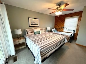A bedroom with two beds, a ceiling fan, a framed picture on the wall, and a window with blinds.