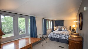 Un dormitorio con cama, mesitas de noche, un escritorio, una silla y una ventana con cortinas.
