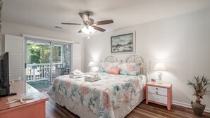 Quarto com cama, mesas de cabeceira, ventilador de teto, televisão e varanda.