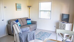A living room with a sofa, armchair, TV stand, and a window with blinds. - Private Beach Front Cottage unit 3 (Ft Pierce)