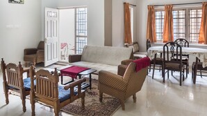 A living room with a sofa, chairs, a dining table with chairs, a patterned rug, and a view through a window with curtains. - GuestHouser 3 BHK Cottage 563f (Ootacamund)