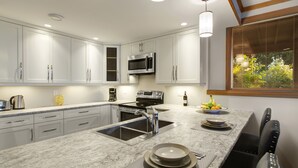 Una cocina moderna con armarios blancos, un lavamanos de acero inoxidable, un microondas integrado y un comedor con mesa y sillas.