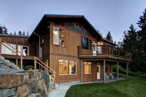 Une cabane en bois dotée d’un balcon, d’un escalier en pierre et d’une cour gazonnée.