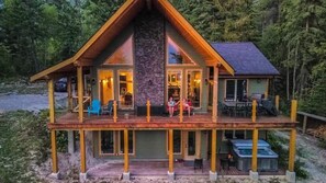 A two-story log cabin with a stone fireplace, outdoor seating, and a hot tub.