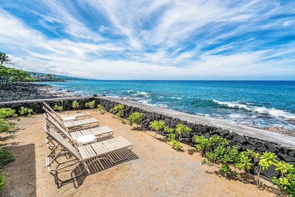 A beachside seating area with lounge chairs and a stone wall. - šļøGround Floor Kona Condo | Pools, AC, Near Town (Kailua Kona)