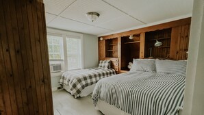 Un dormitorio con dos camas, un armario de madera, una ventana con persianas y un ventilador de techo.