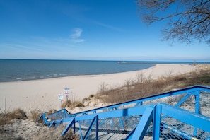 A beach with a blue staircase leading down to the shore, clear skies, and calm waters.