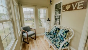 Una habitación acogedora con piso de madera, una silla blanca, un sofá floral y un cartel en la pared que dice "LOVE".