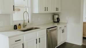 Una cocina moderna con armarios blancos, lavavajillas de acero inoxidable y cafetera.
