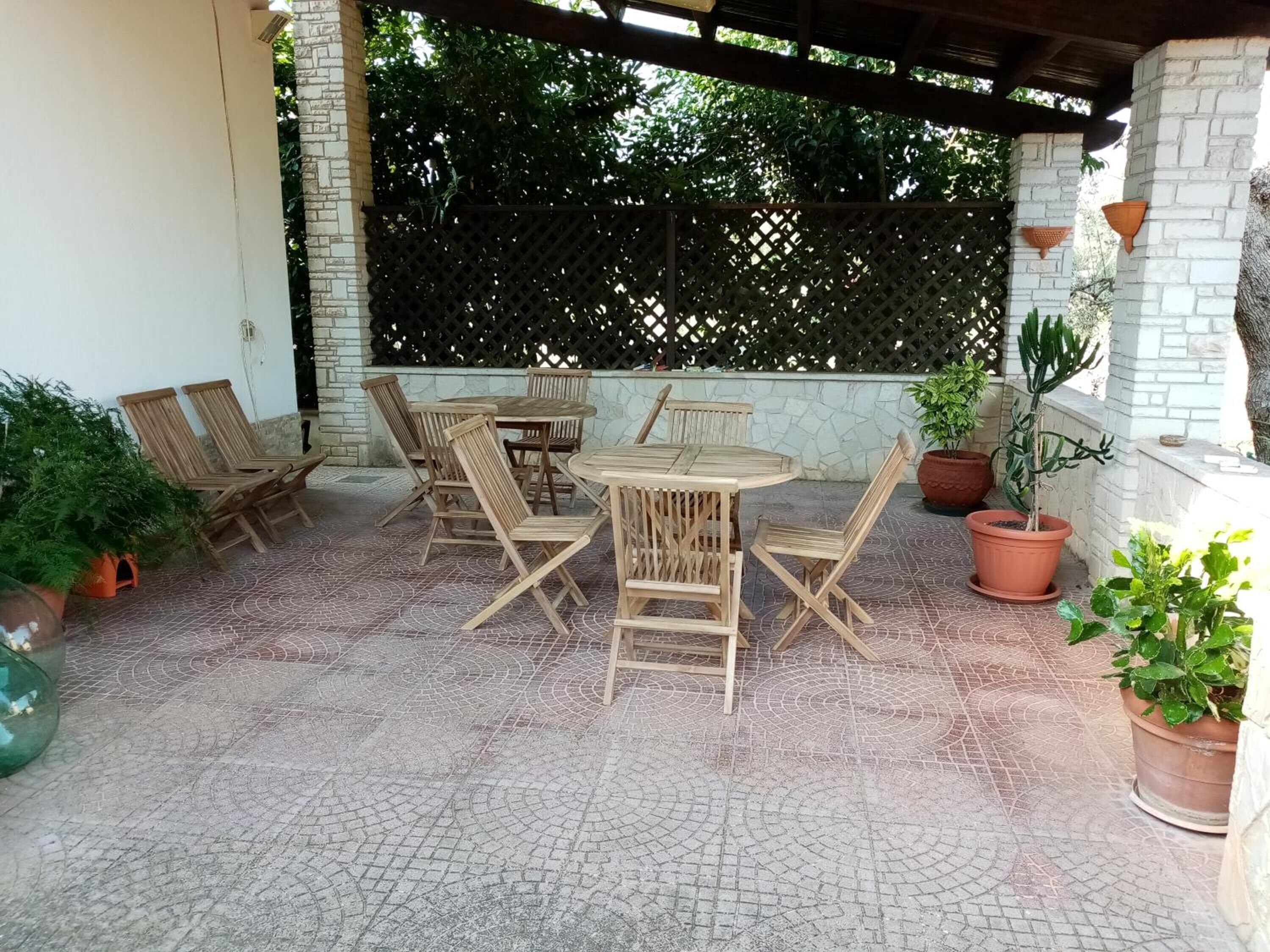 Une terrasse extérieure avec une table et des chaises en bois, entourée de plantes en pot et d’une clôture en treillis.