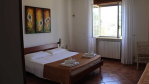 A hotel room with a bed, a radiator, a window with curtains, and a chair.