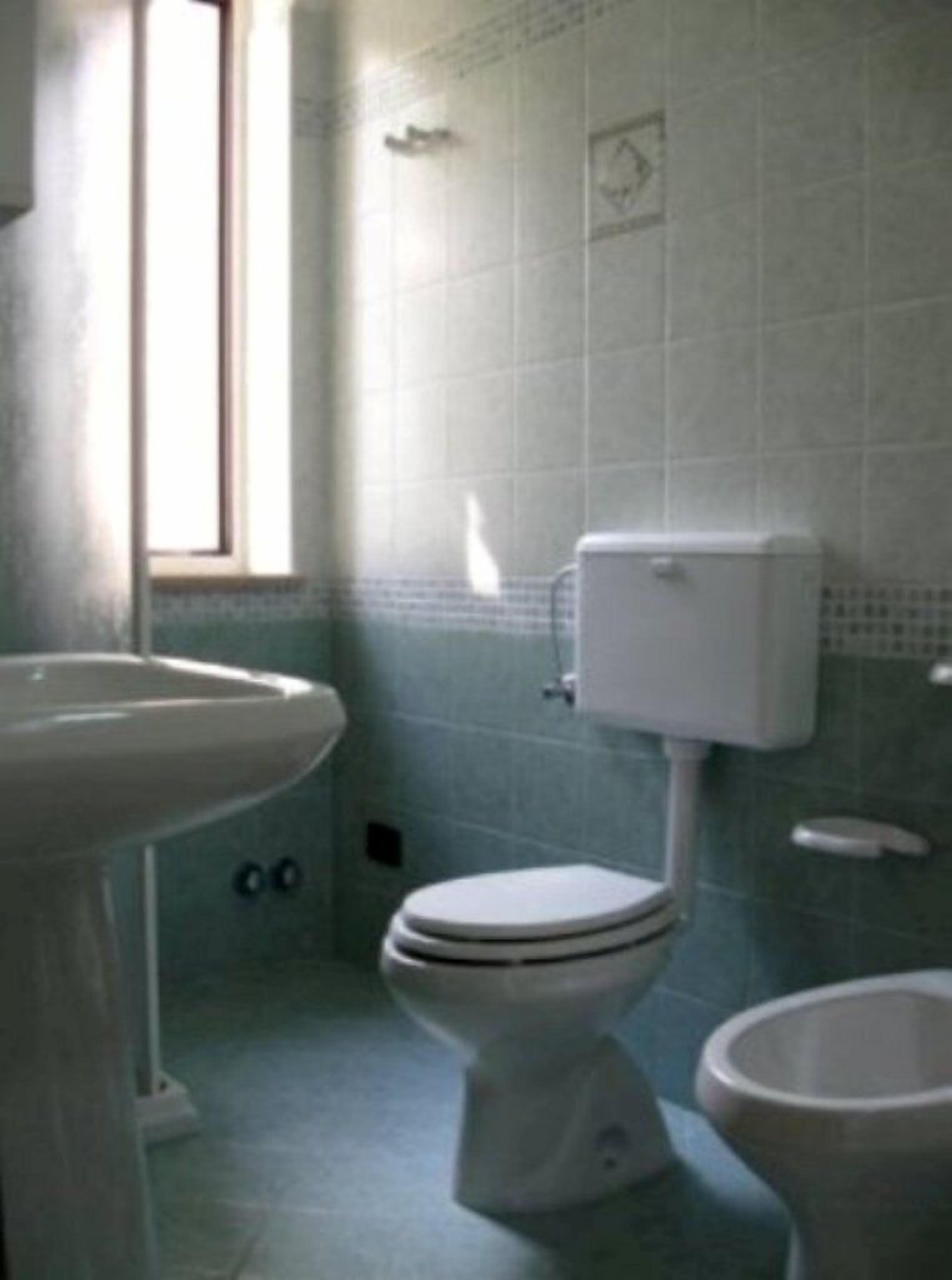 A bathroom with a toilet, sink, and a window.