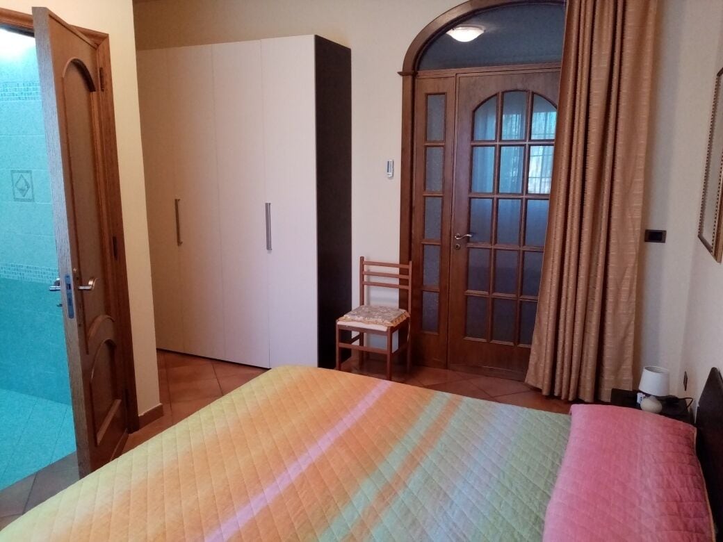 Un dormitorio con cama, una silla, armario y una puerta con paneles de vidrio.