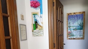 A hallway with a wooden door, a painting of a pink tree, a certificate, and a potted plant.