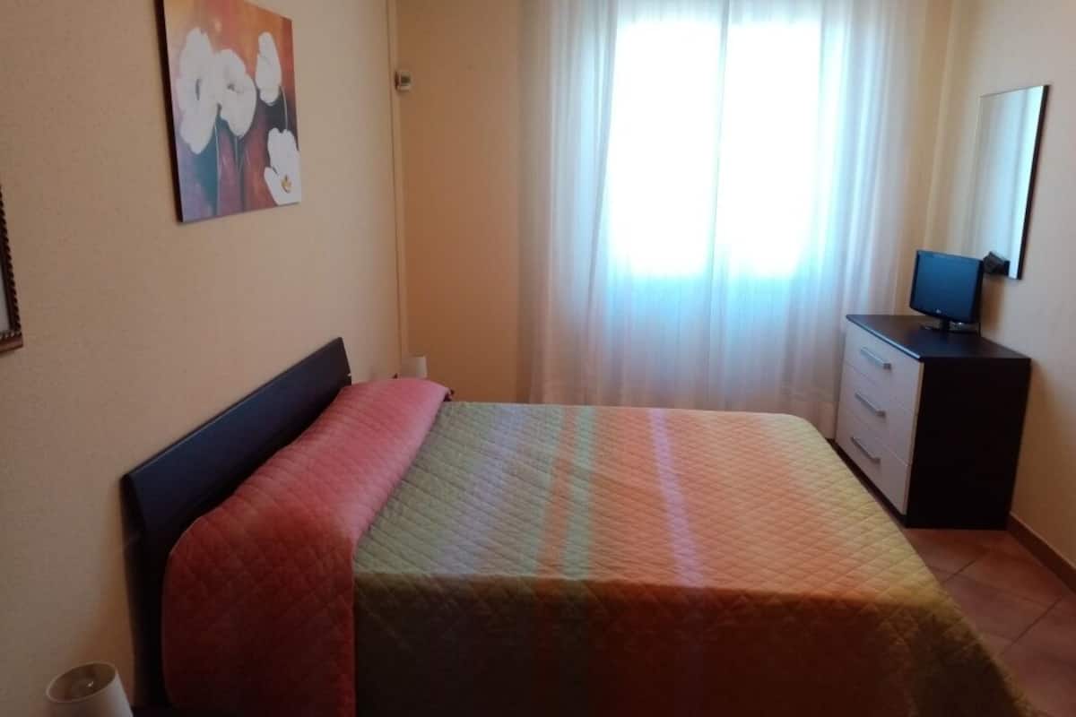 A bedroom with a bed, a dresser, a television, and a painting on the wall.