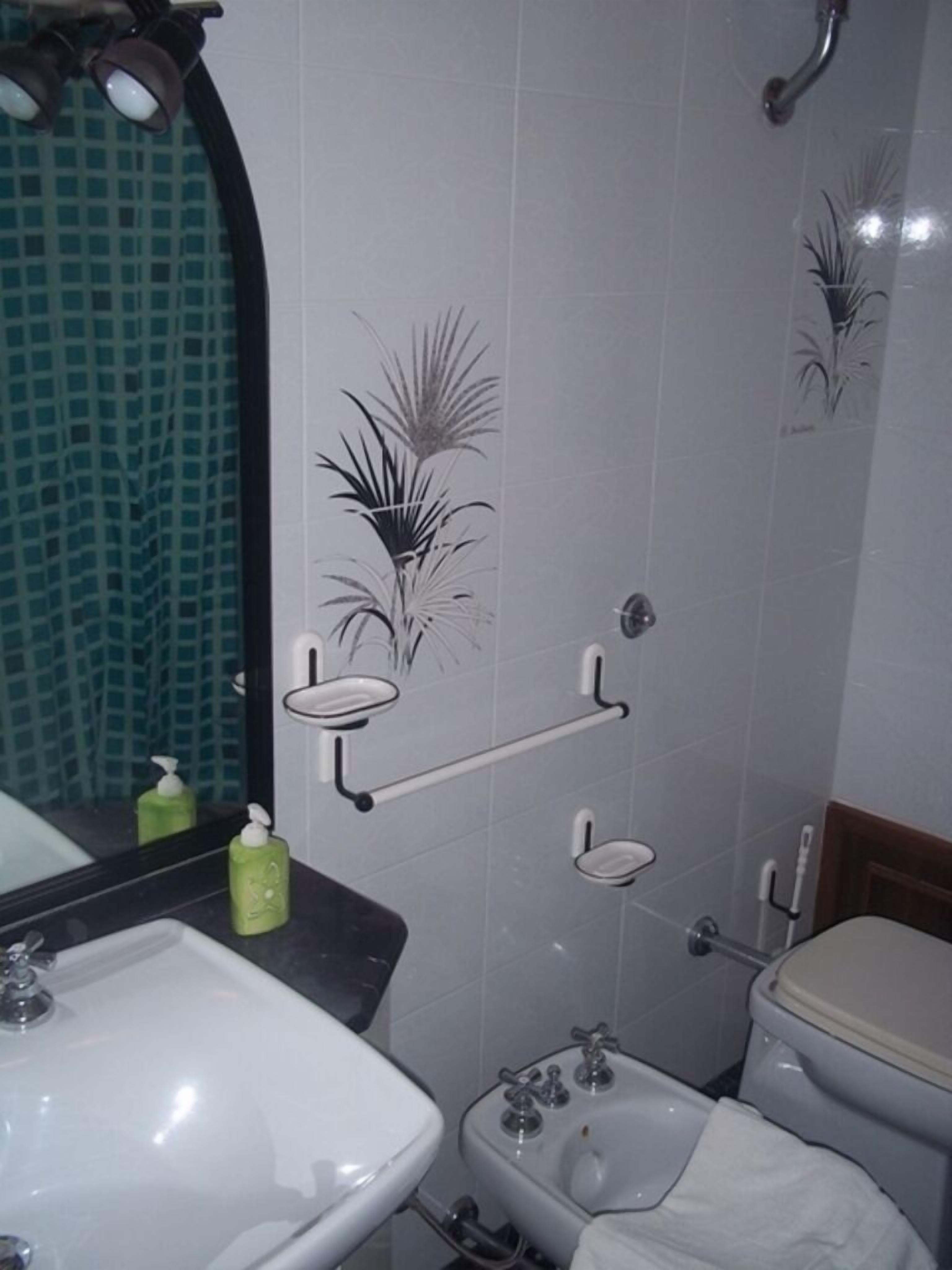 A bathroom with a white sink, toilet, and shower area. There are decorative tiles on the walls and a mirror above the sink.