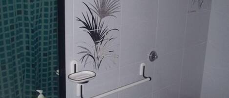 A bathroom with a white sink, toilet, and shower area. There are decorative tiles on the walls and a mirror above the sink.