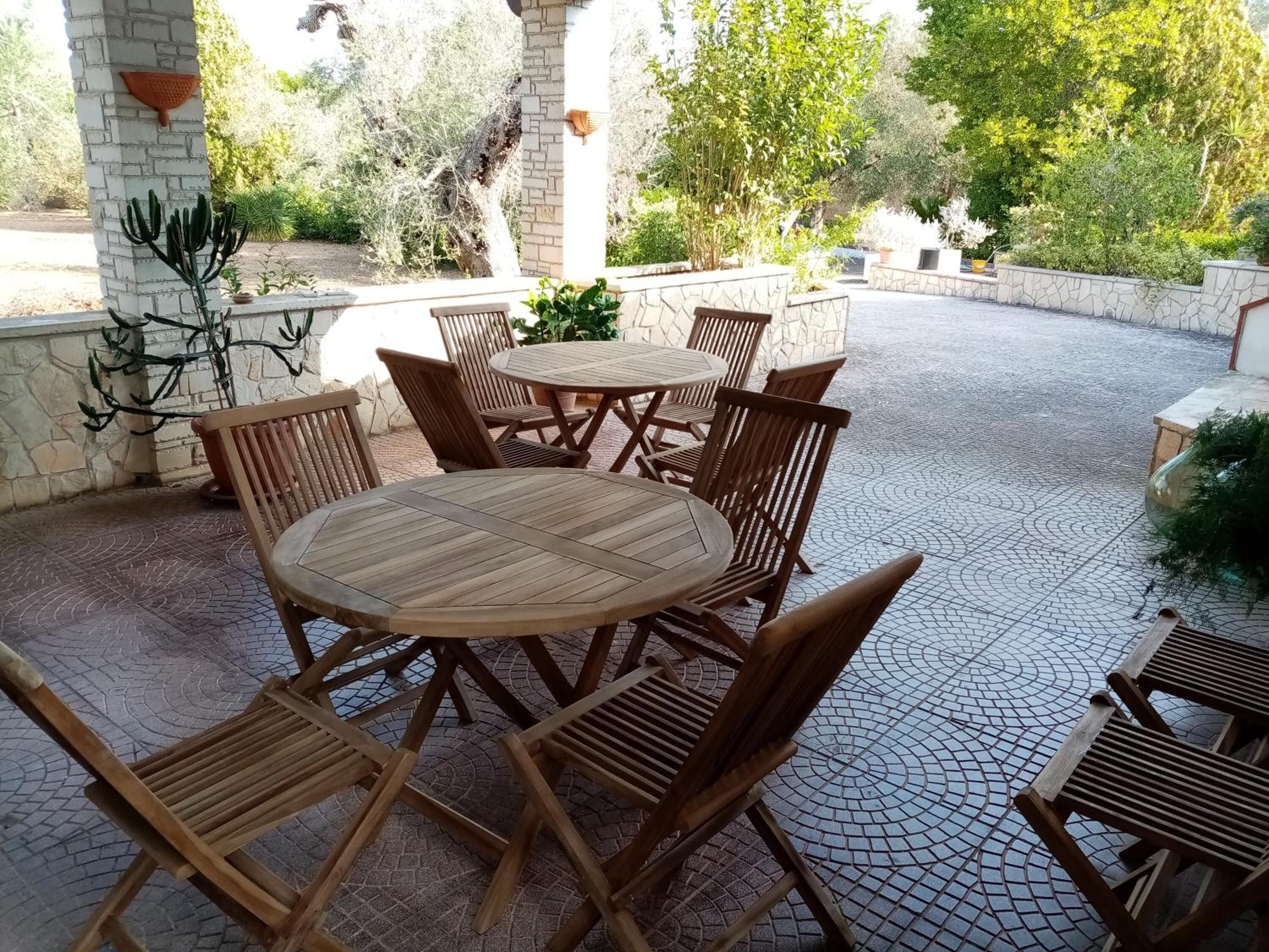 Ein Patio mit einem runden Holztisch und sechs Stühlen, umgeben von Steinmauern und Blumentöpfen.