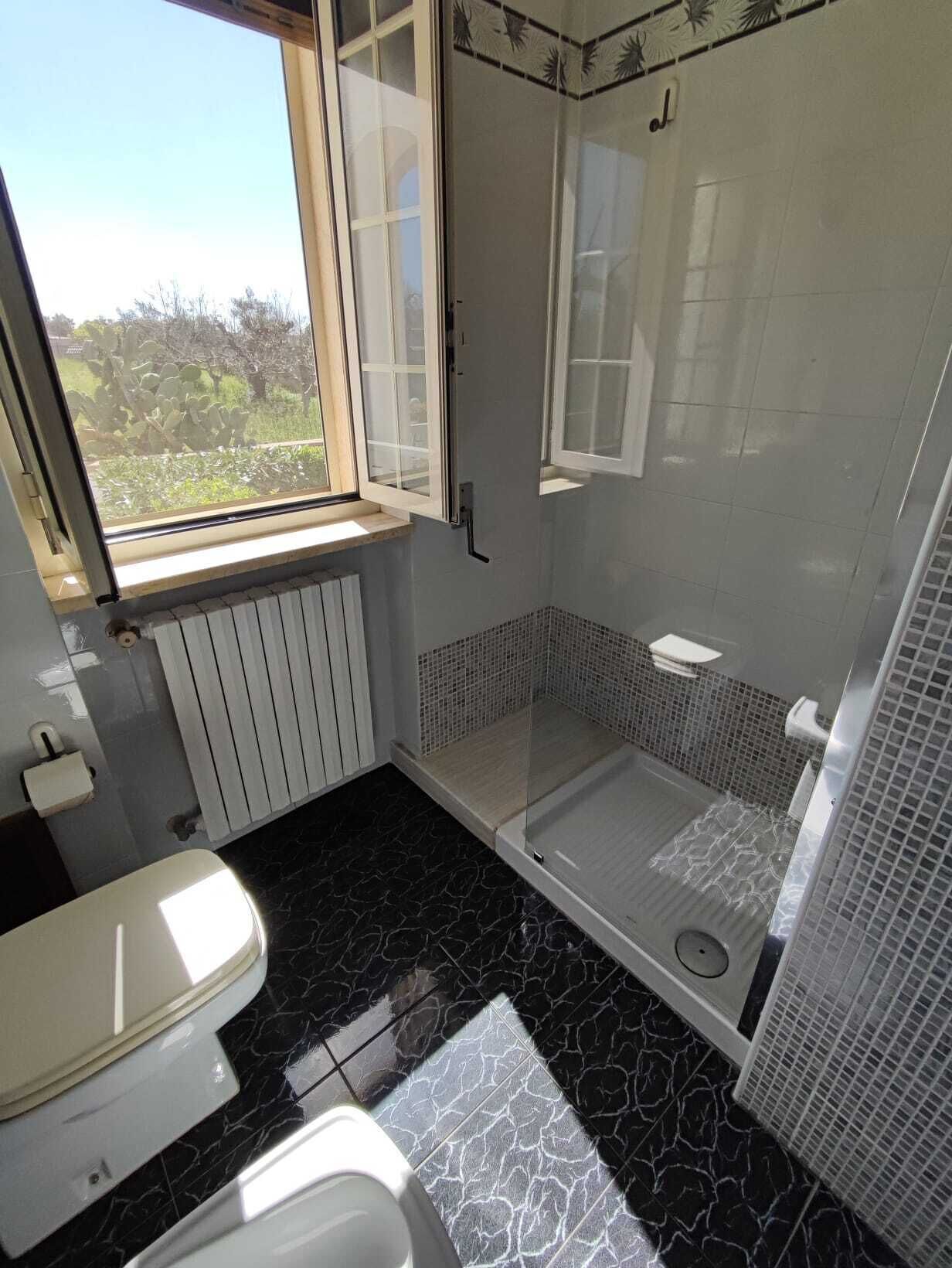 Ein Badezimmer mit Dusche, Toilette und einem Fenster mit Blick auf Grünflächen.