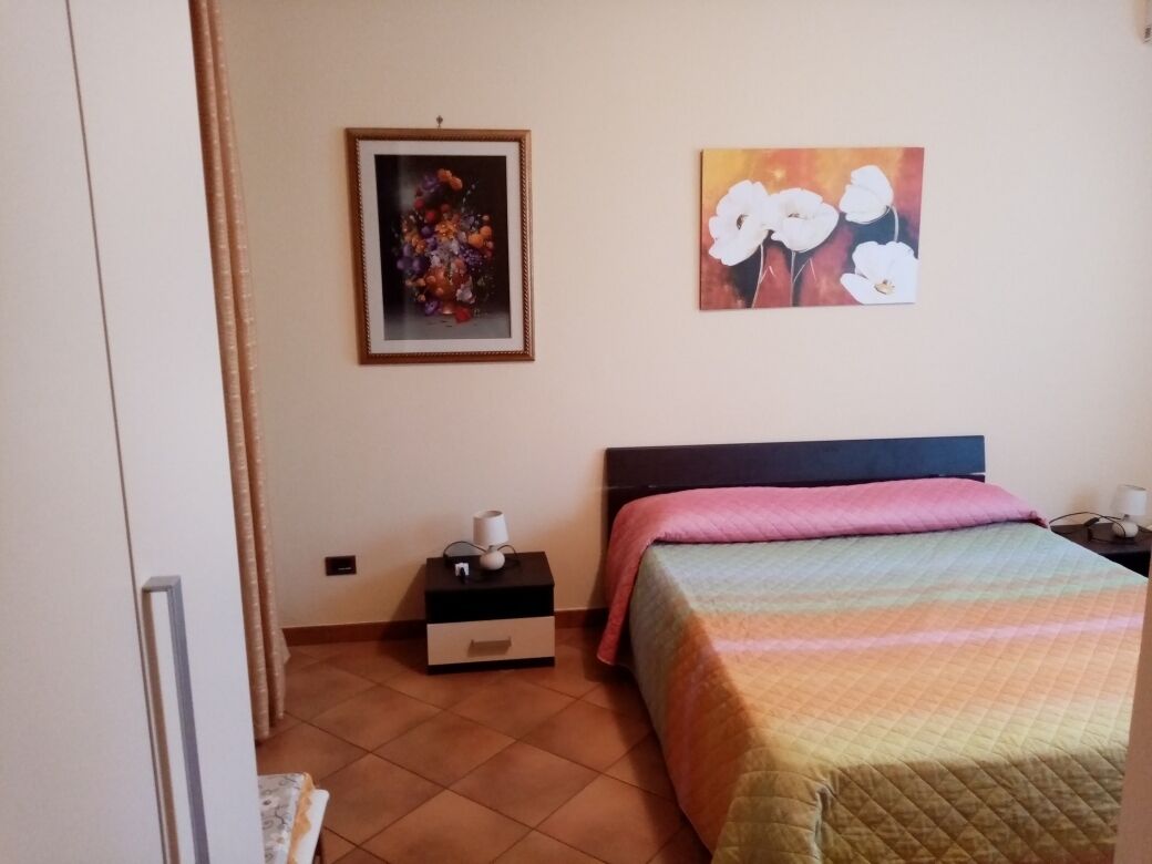 Un dormitorio con una cama, una mesita de noche, un cajón y dos cuadros en la pared.
