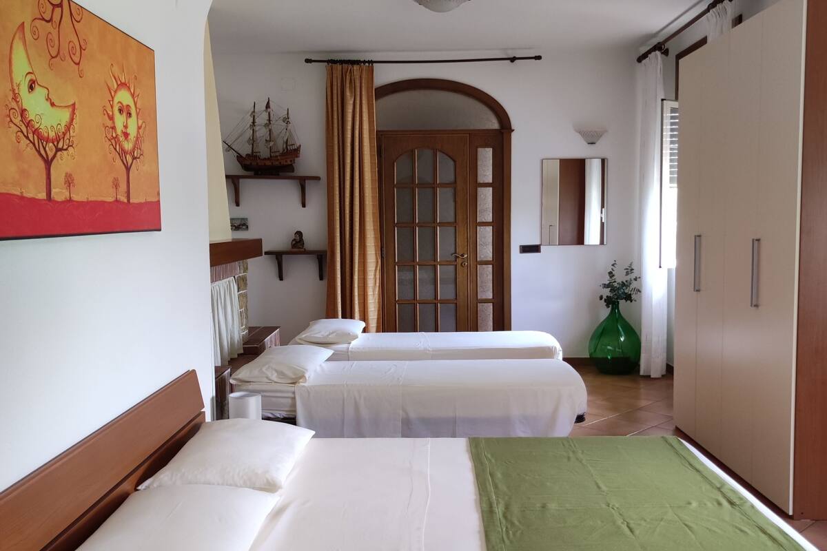 A hotel room with two beds, a wooden headboard, a green throw blanket, a large painting, a ship model, and a green vase.