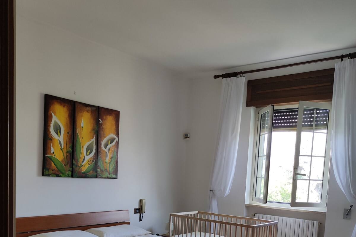 A bedroom with a wooden bed, a crib, a window with curtains, and a radiator.