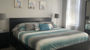 Un dormitorio con cama, mesitas de noche, ventilador de techo y tres cuadros colgados en la pared.